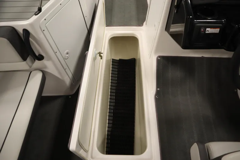 Slide: The Image of 2021 Yamaha Boats 190 AR storage compartment with black mat, adjacent seating and console. - 27