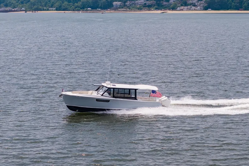 Slide: The Image of 2025 MJM 3 boat cruising on water with American flag, scenic shoreline background. - 15