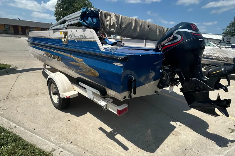 Slide: The Image of 1999 Crestliner Rampage 2000 boat with Evinrude motor on trailer, parked outdoors. - 2