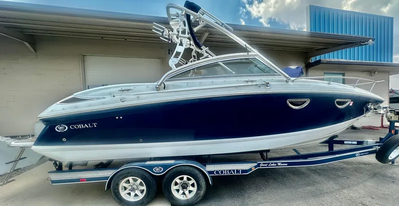 Slide: The Image of 2012 Cobalt 243 boat on trailer, blue and white, parked outdoors. - 2