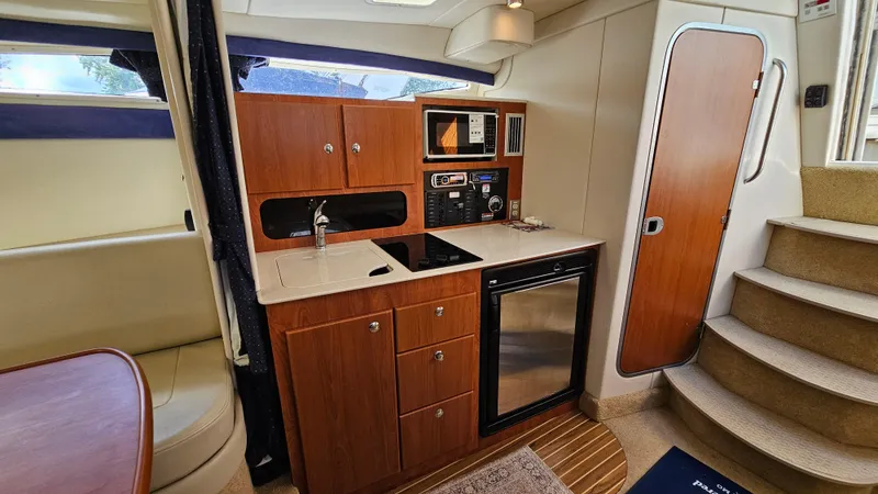 Slide: The Image of 2009 Bayliner 340 SB yacht interior with kitchenette, featuring wood cabinets, sink, and compact appliances. - 20