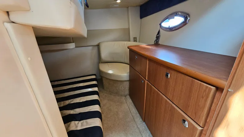 Slide: The Image of 2009 Bayliner 340 SB cabin interior with striped bedding, wooden cabinets, and porthole window. - 24