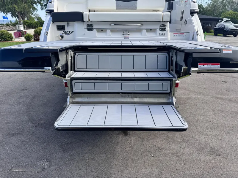 Slide: The Image of 2025 Chaparral 307 SSX boat with open rear storage compartments on a sunny day. - 19