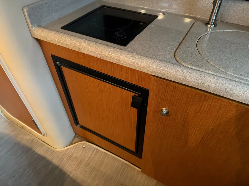 Slide: The Image of 2004 Cruisers Yachts 280 Express galley with stove, sink, and wooden cabinetry. - 23