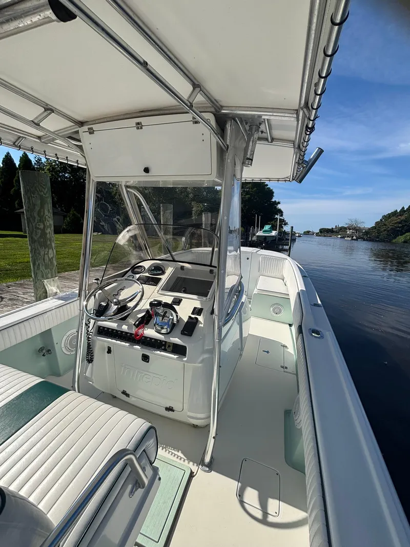 Slide: The Image of 1998 Intrepid 327 Cuddy boat interior with steering console, docked by a serene waterway. - 16