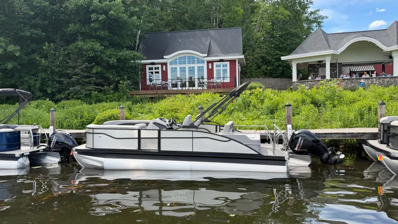 Slide: The Image of A Barletta Aria 22 UC pontoon boat is docked on the water in front of a picturesque house. - 0