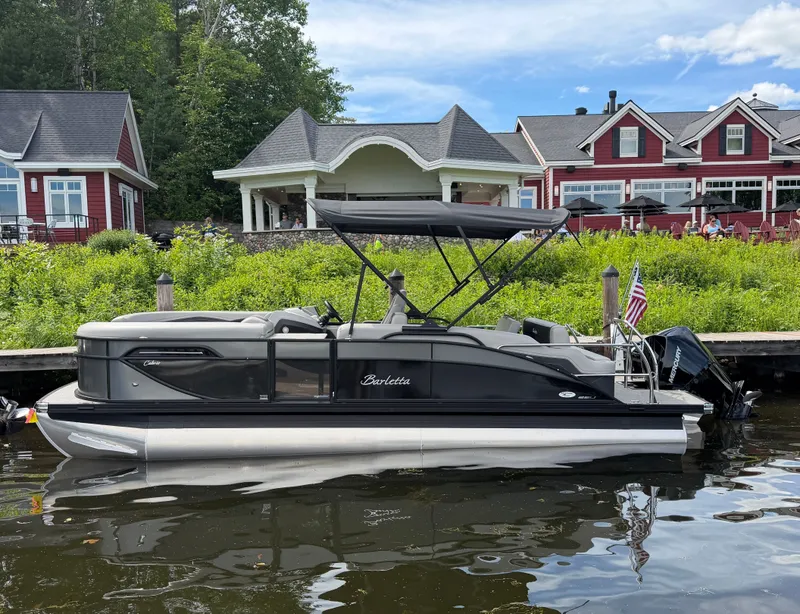 Slide: The Image of A Barletta Cabrio 22 U pontoon boat docked by the shore with picturesque houses in the background. - 0