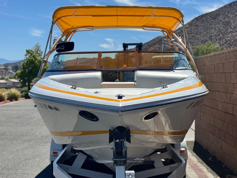 Slide: The Image of 2006 Cobalt 246 boat with yellow canopy on trailer, parked near brick wall. - 2