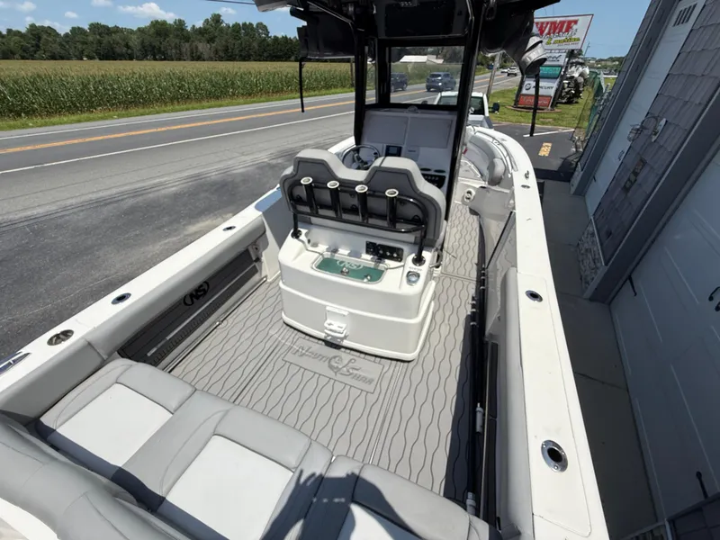 Slide: The Image of 2022 NauticStar 2602 Legacy boat interior with seating and console, parked near a road. - 14