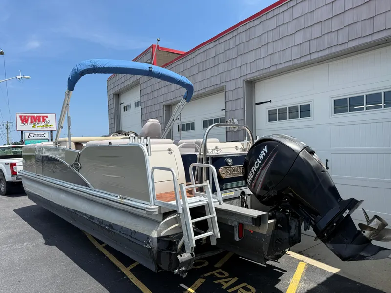 Slide: The Image of 2014 Avalon 2585 Catalina Bar Tri Toon boat with Mercury engine, parked outside a garage. - 7