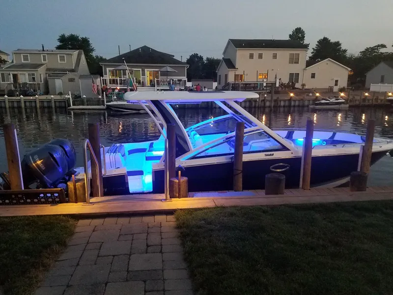 Slide: The Image of 2020 Chaparral 300 OSX boat docked with blue interior lights at dusk. - 4
