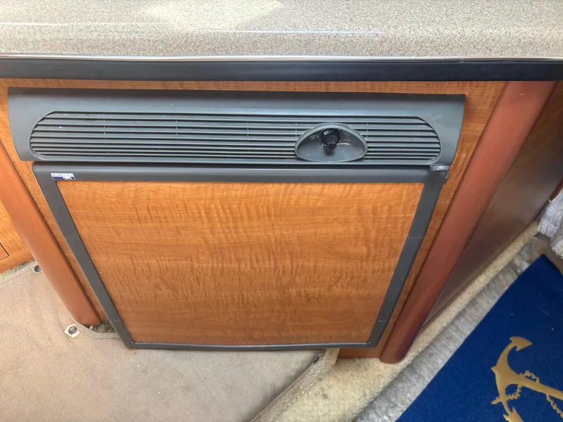 Slide: The Image of 2006 Sea Ray 260 Sundancer cabin interior with a wooden panel and compact refrigerator. - 22