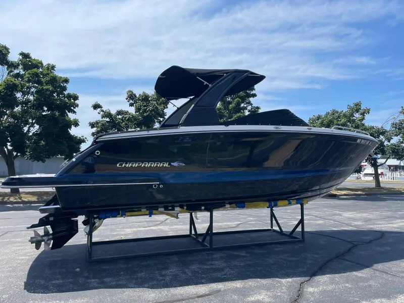 Slide: The Image of 2018 Chaparral 267 SSX boat on display, black hull, sunny day, trees in background. - 2