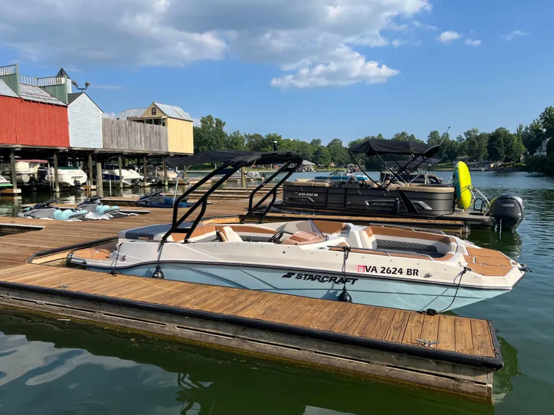 The Image of 2025 Starcraft SVX 231 IO boat docked at a scenic marina under a blue sky. - 0