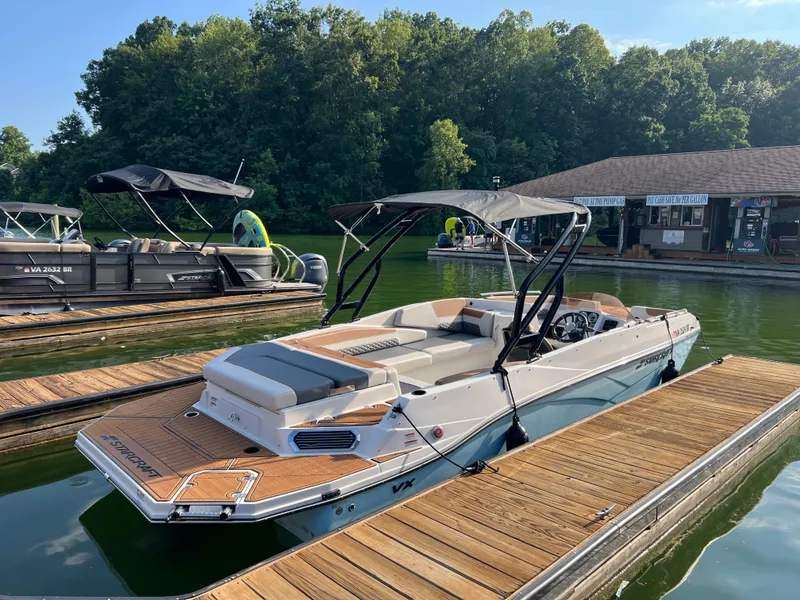 Slide: The Image of 2025 Starcraft SVX 231 IO boat docked on a sunny day, surrounded by lush greenery. - 1