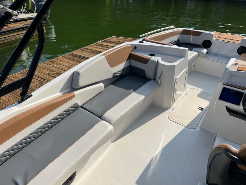 Slide: The Image of 2025 Starcraft SVX 231 IO boat interior with cushioned seating and storage, docked by the water. - 11