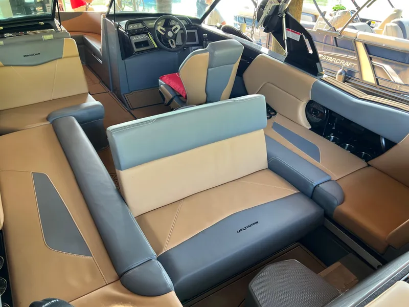 Slide: The Image of 2025 MasterCraft NXT23 boat interior with beige and gray seating, modern dashboard, and steering wheel. - 10