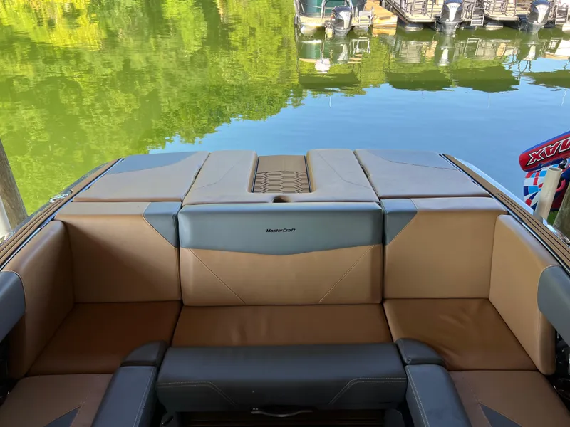 Slide: The Image of 2025 MasterCraft NXT23 boat interior with tan and gray seating by a calm lake. - 12