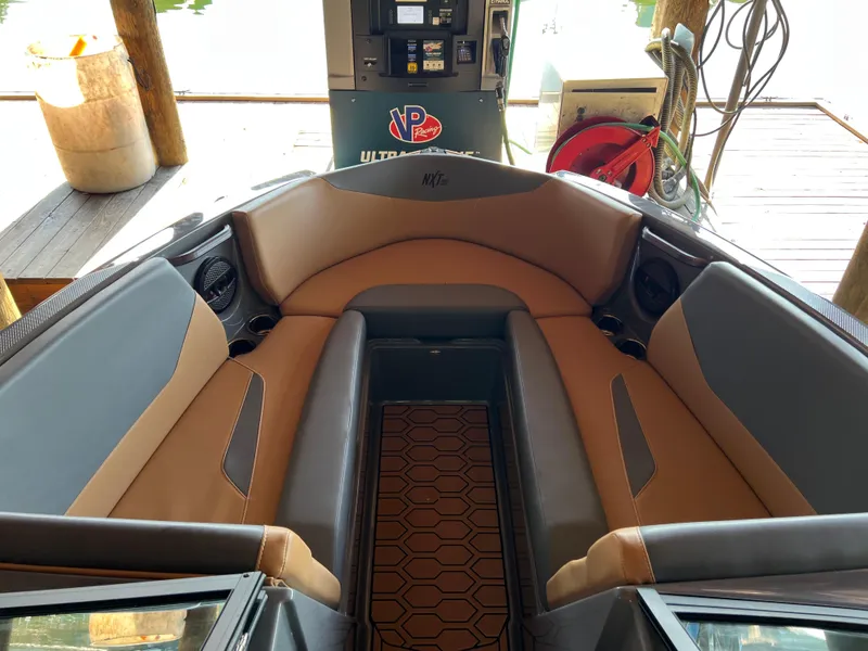 Slide: The Image of 2025 MasterCraft NXT23 boat interior with tan and gray seating, docked near a fuel station. - 8