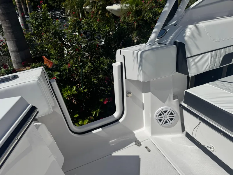 Slide: The Image of 2026 Blackfin 272 DC boat interior with white seating and speaker, surrounded by lush greenery. - 14