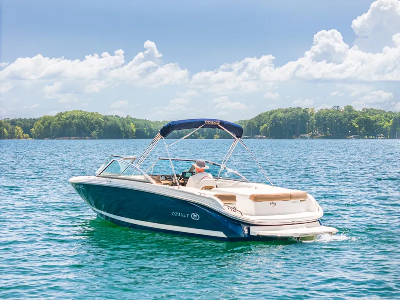 Slide: The Image of 2016 Cobalt 200 boat cruising on a sunny lake with lush green shoreline. - 3