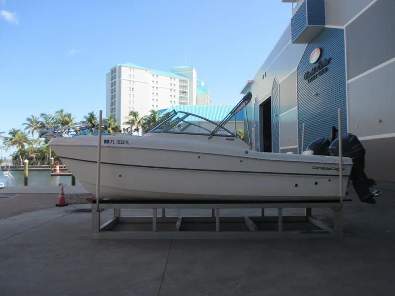 Slide: The Image of 2013 Carolina Cat 230 DC boat on a dock, with a marina and palm trees in the background. - 3