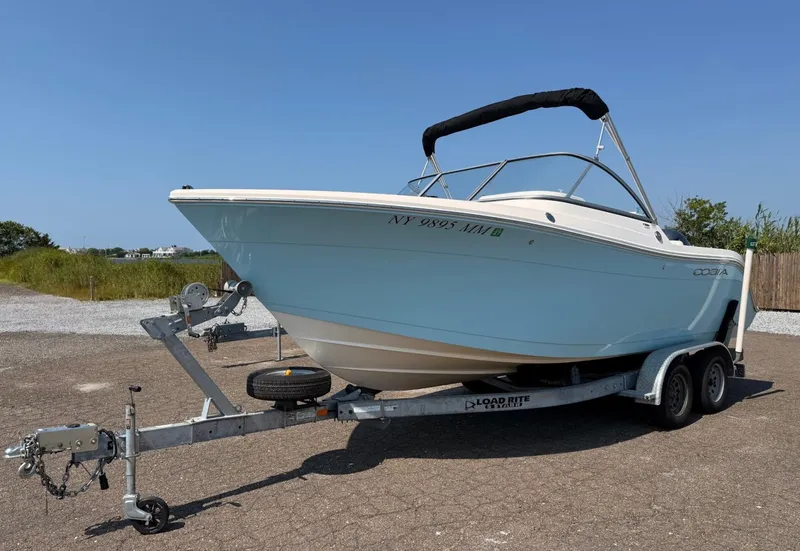 Slide: The Image of 2017 Cobia 220 Dual Console boat on trailer, parked outdoors under clear blue sky. - 0