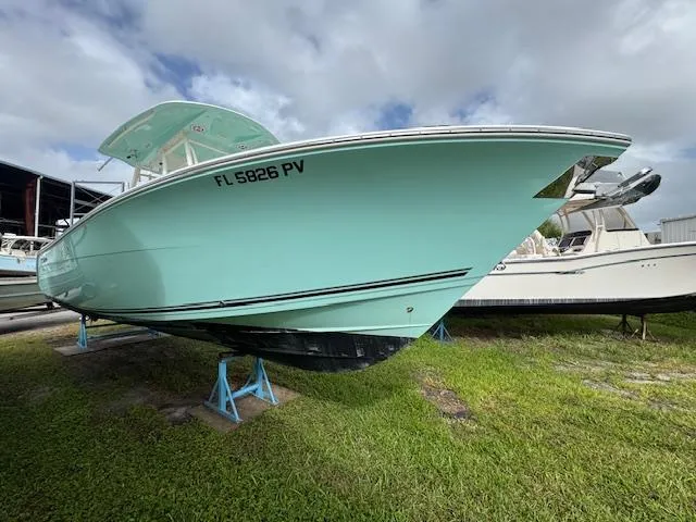 Slide: The Image of 2015 Cobia 296 Center Console boat on stands, light blue hull, grassy area. - 0