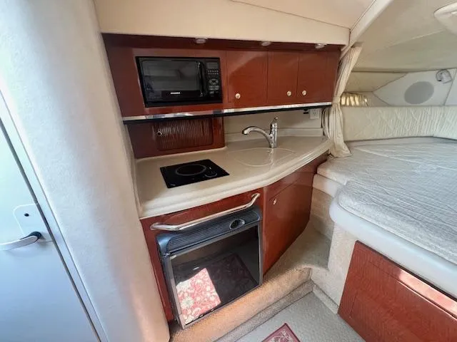 Slide: The Image of 2003 Sea Ray 290 Amberjack cabin with kitchenette, featuring microwave, stove, sink, and cozy sleeping area. - 12