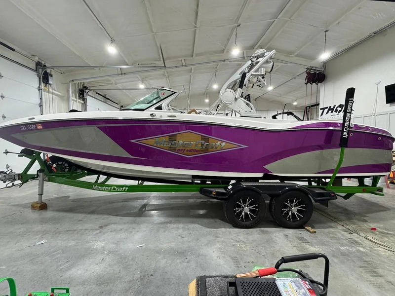 Slide: The Image of 2016 MasterCraft X26 boat in a garage, purple and silver design on a green trailer. - 1