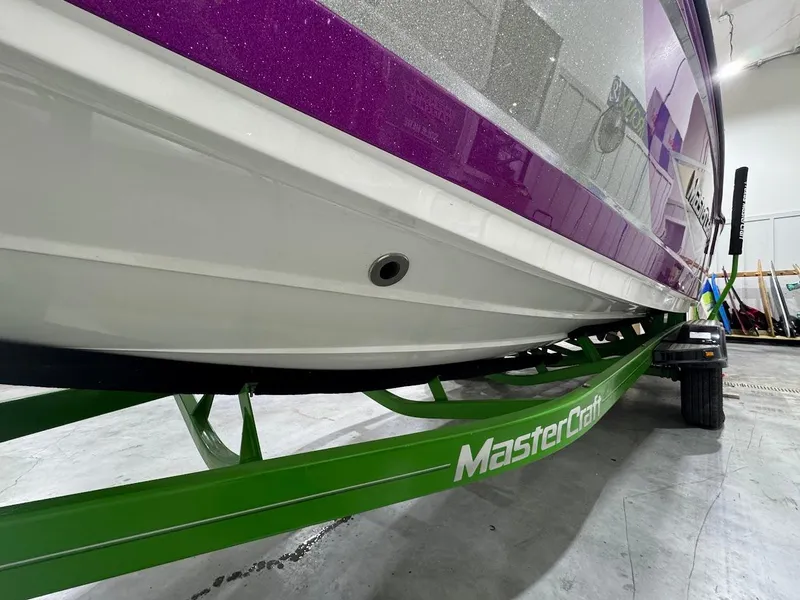 Slide: The Image of 2016 MasterCraft X26 boat on green trailer in indoor setting. - 10