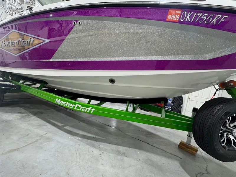 Slide: The Image of 2016 MasterCraft X26 boat with purple and silver design on a green trailer. - 11