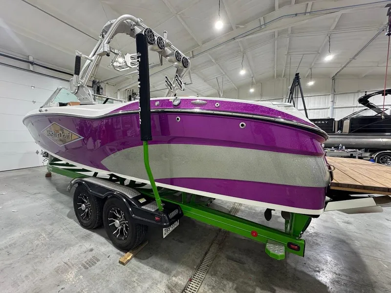 Slide: The Image of 2016 MasterCraft X26 boat in vibrant purple and silver, displayed indoors on a trailer. - 2