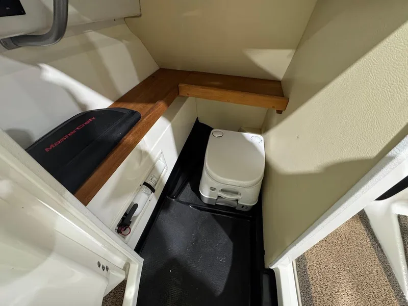 Slide: The Image of 2016 MasterCraft X26 interior with compact toilet and wooden shelf. - 21