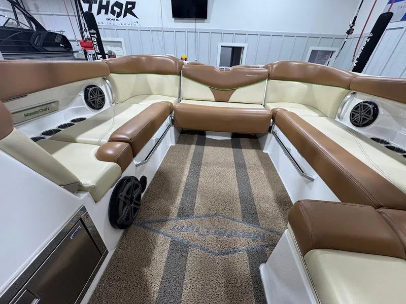 Slide: The Image of 2016 MasterCraft X26 boat interior with brown and cream seating, featuring speakers and cup holders. - 24
