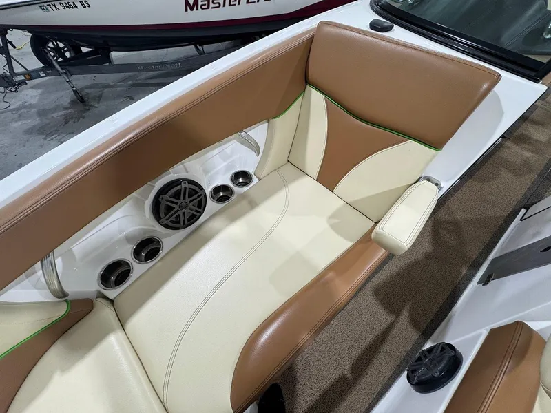 Slide: The Image of 2016 MasterCraft X26 boat interior with tan and cream seating, cup holders, and speaker. - 33