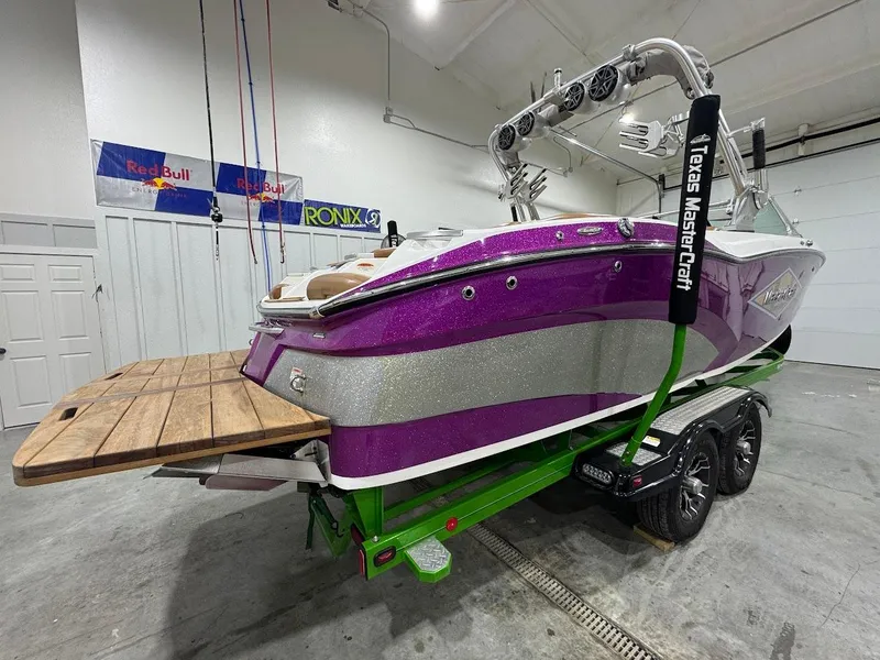 Slide: The Image of 2016 MasterCraft X26 boat in vibrant purple and silver, displayed indoors on a green trailer. - 5