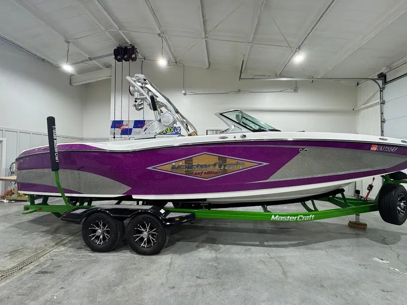 Slide: The Image of 2016 MasterCraft X26 boat with purple and silver design on a green trailer in a garage. - 6