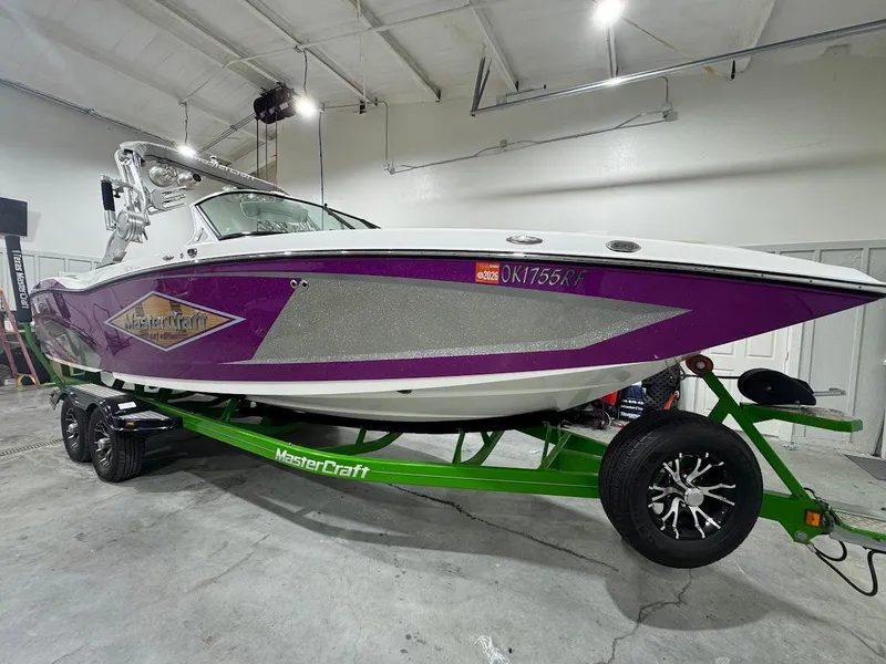 Slide: The Image of 2016 MasterCraft X26 boat with purple and silver design on a green trailer in a garage. - 7