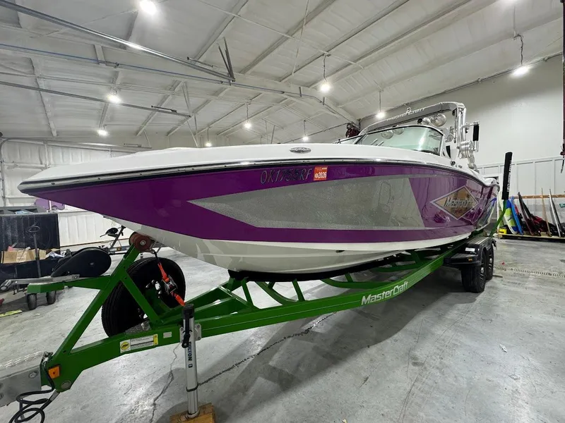Slide: The Image of 2016 MasterCraft X26 boat with purple hull on green trailer in a spacious garage. - 9