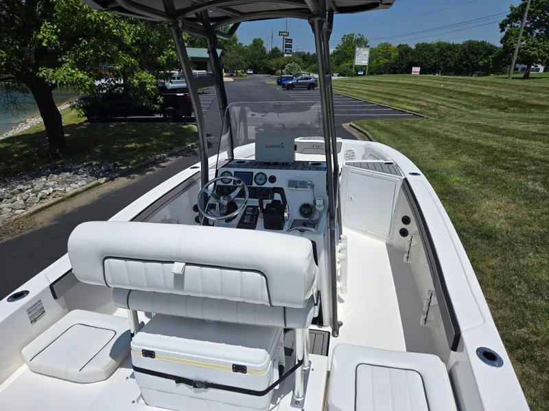 Slide: The Image of 2018 Yamaha Boats 210 FSH Sport interior with steering console and seating, parked outdoors. - 10
