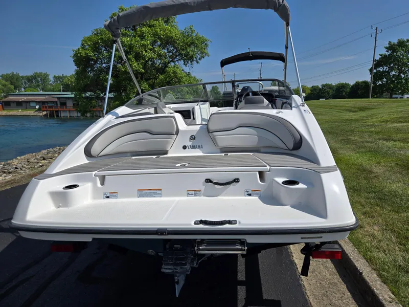 Slide: The Image of 2021 Yamaha Boats SX190 on trailer, rear view, near water and grassy area. - 2