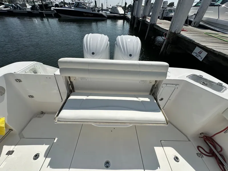 Slide: The Image of 2023 Edgewater 285CC boat with foldable seating at the stern, docked at a marina. - 19