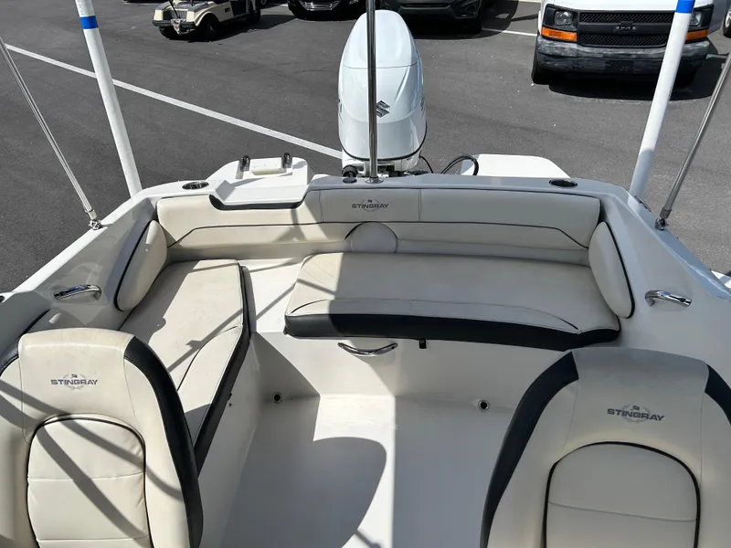Slide: The Image of 2021 Stingray 191 DC boat interior with seating and motor, parked in a lot. - 10