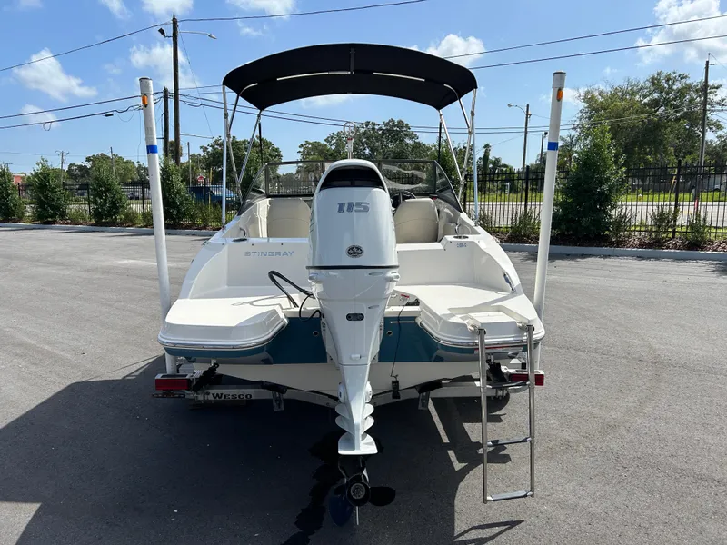Slide: The Image of 2021 Stingray 191 DC boat with outboard motor and canopy, parked on pavement. - 2