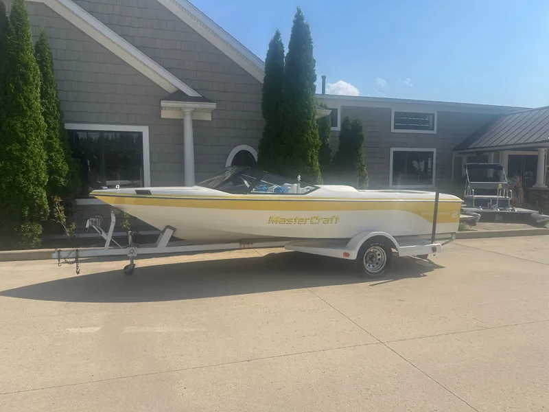 The Image of 1990 MasterCraft Prostar190 boat on trailer, parked outside a building on a sunny day. - 1