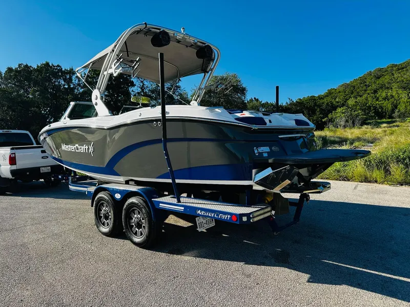 Slide: The Image of 2018 MasterCraft X23 boat on trailer, parked outdoors under clear blue sky. - 10