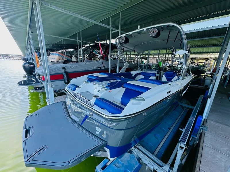 Slide: The Image of 2018 MasterCraft X23 boat docked, featuring blue and white seating under a covered marina. - 14