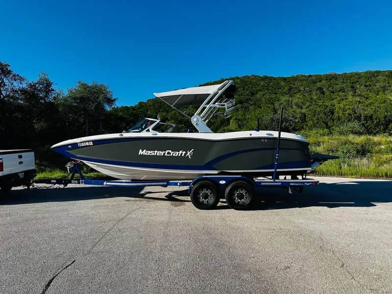 Slide: The Image of 2018 MasterCraft X23 boat on trailer, parked outdoors with lush greenery background. - 8