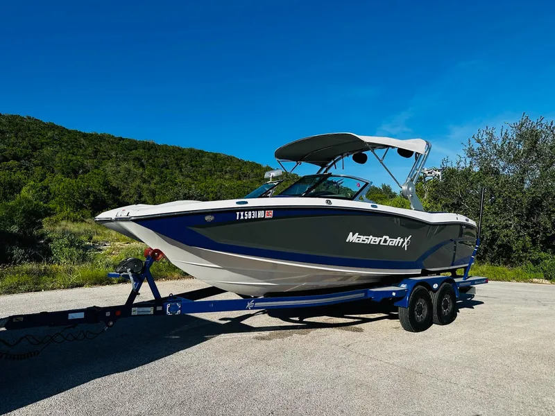 Slide: The Image of 2018 MasterCraft X23 boat on trailer, parked outdoors under clear blue sky. - 9